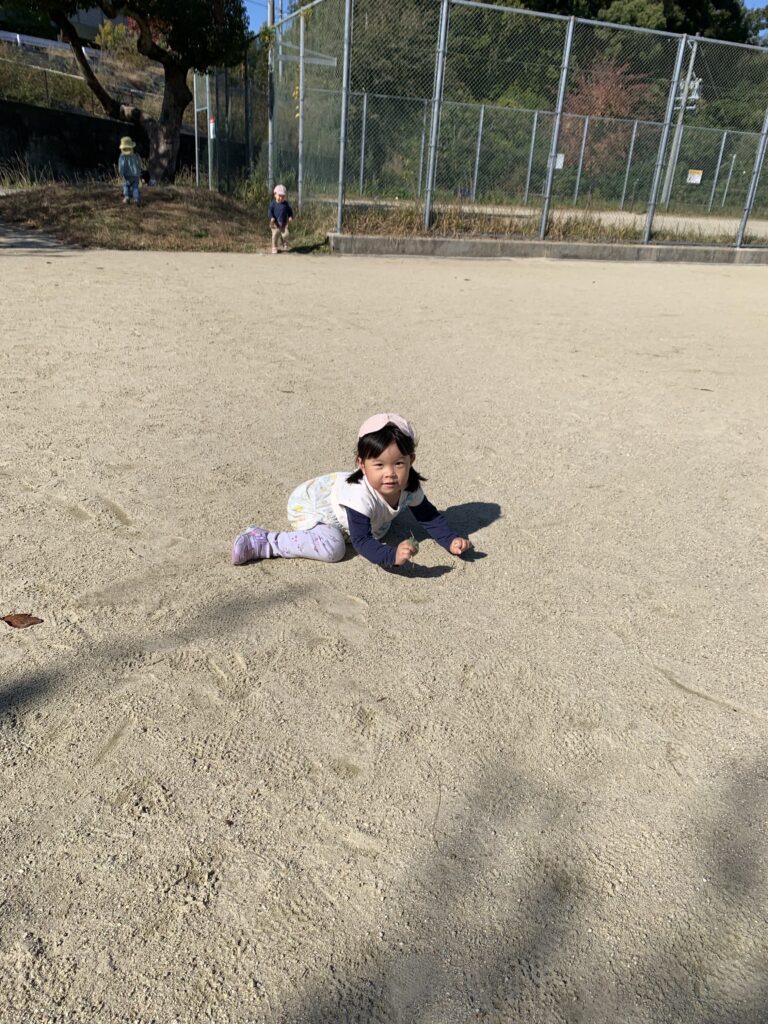 公園の砂の上で横になる園児